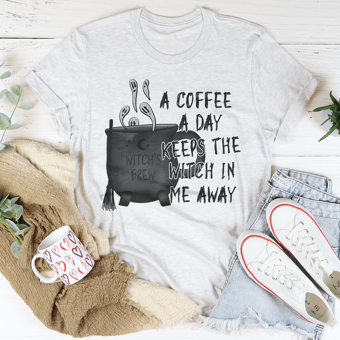 A stylish black t-shirt with the phrase 'A Coffee A Day Keeps The Witch In Me Away' printed in white, showcasing its soft fabric and durable stitching.