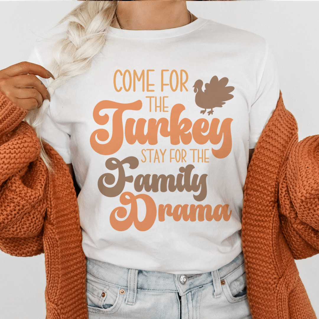 A comfortable and durable t-shirt featuring the phrase 'Come For The Turkey Stay For The Family Drama' in a stylish font, perfect for family gatherings.