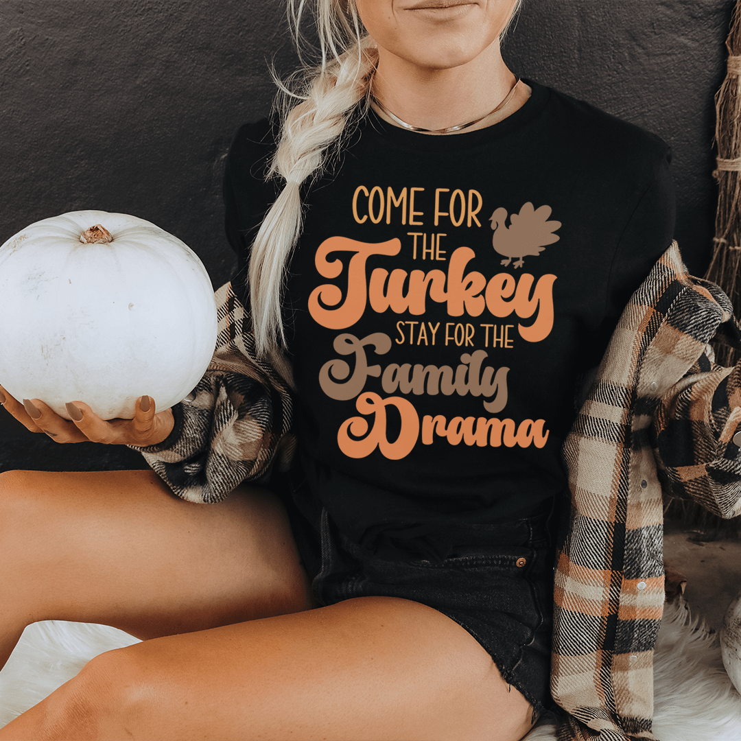 A comfortable and durable t-shirt featuring the phrase 'Come For The Turkey Stay For The Family Drama' in a stylish font, perfect for family gatherings.