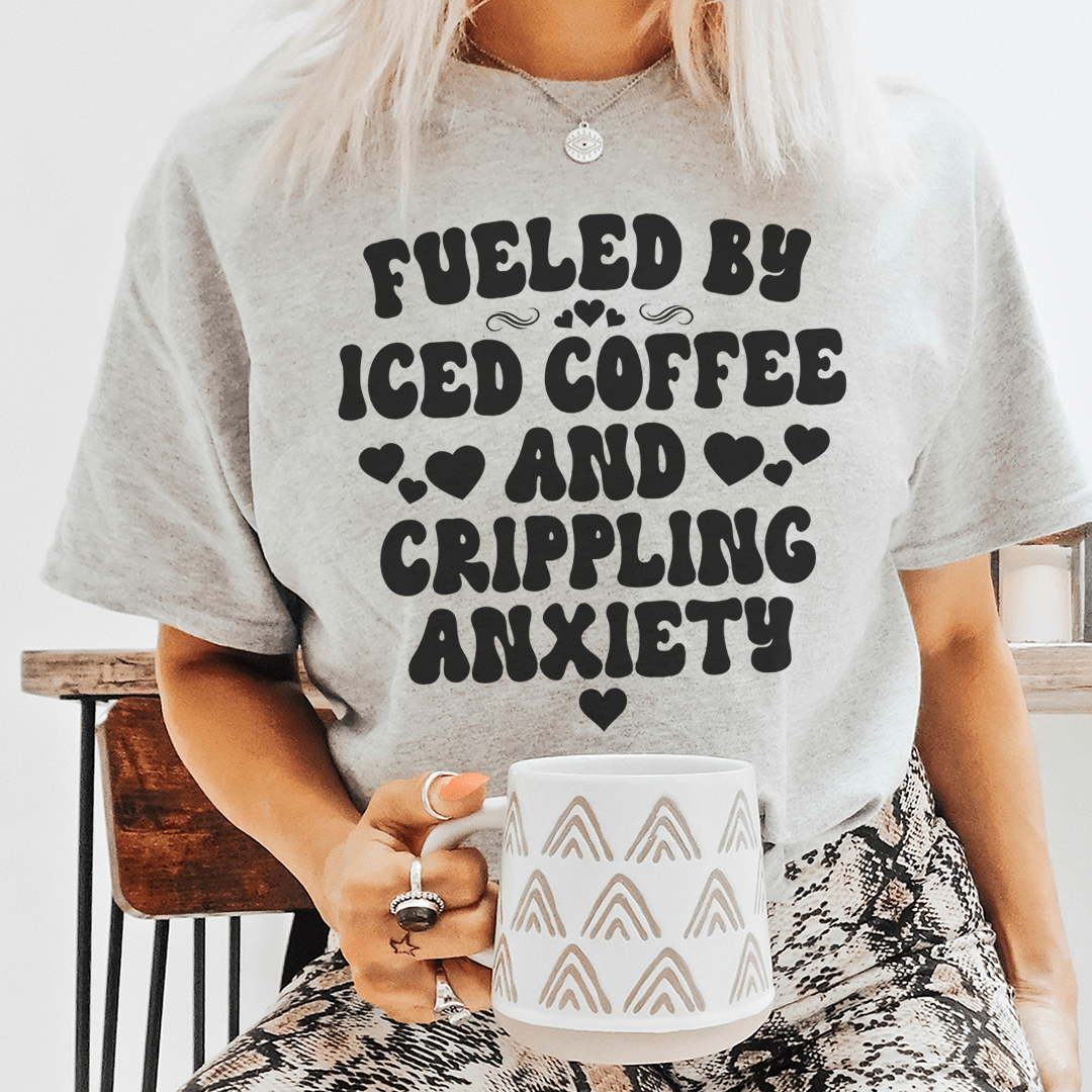 A stylish black t-shirt featuring the phrase 'Fueled By Iced Coffee And Crippling Anxiety' printed in bold, eye-catching letters.