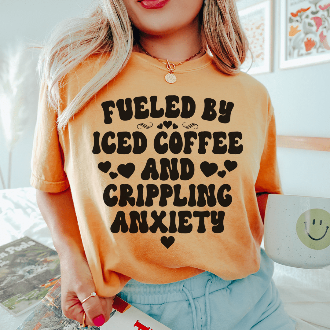 A stylish black t-shirt featuring the phrase 'Fueled By Iced Coffee And Crippling Anxiety' printed in bold, eye-catching letters.