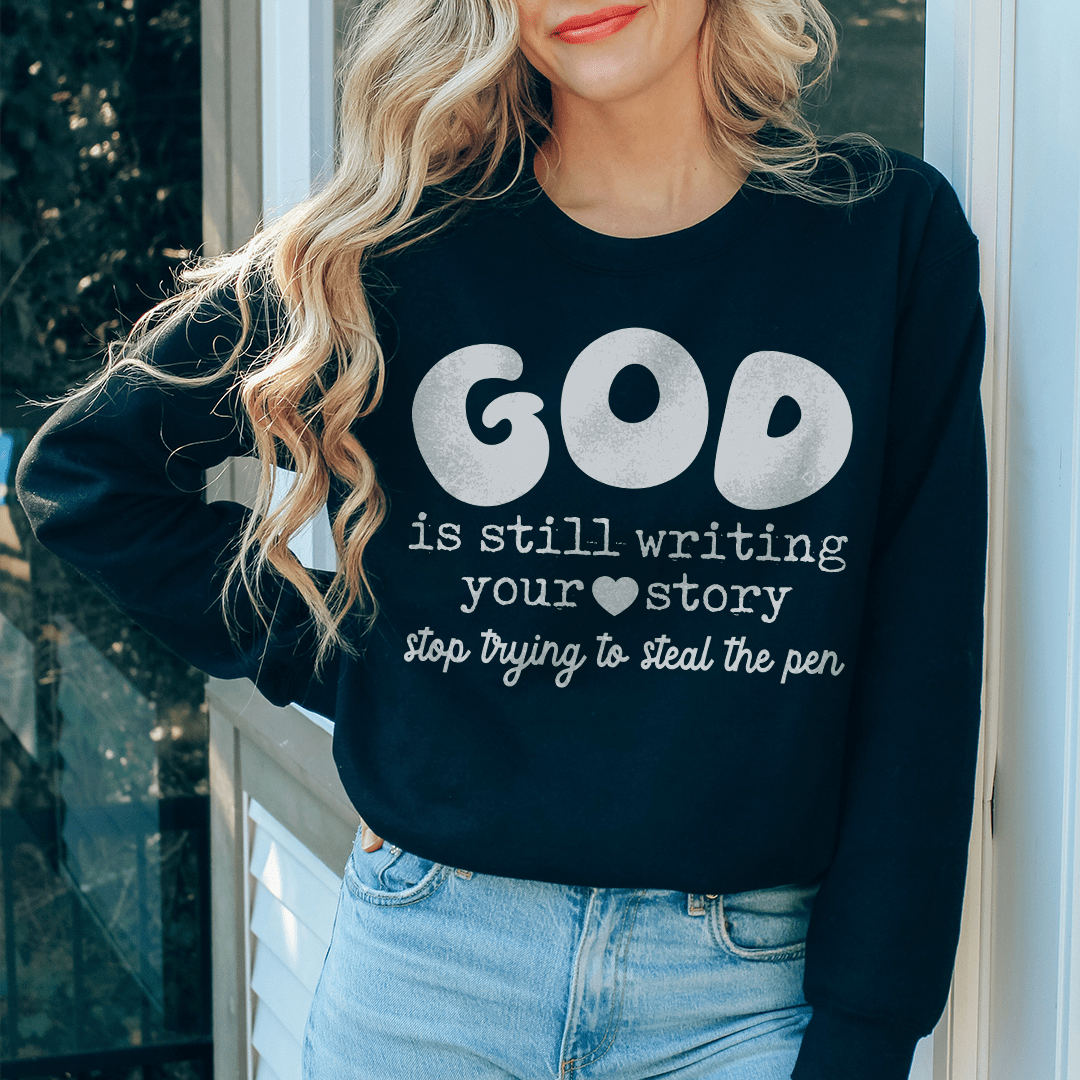 A cozy sweatshirt featuring the phrase 'God Is Still Writing Your Story', designed by top artists, made from a warm cotton/poly fleece blend.