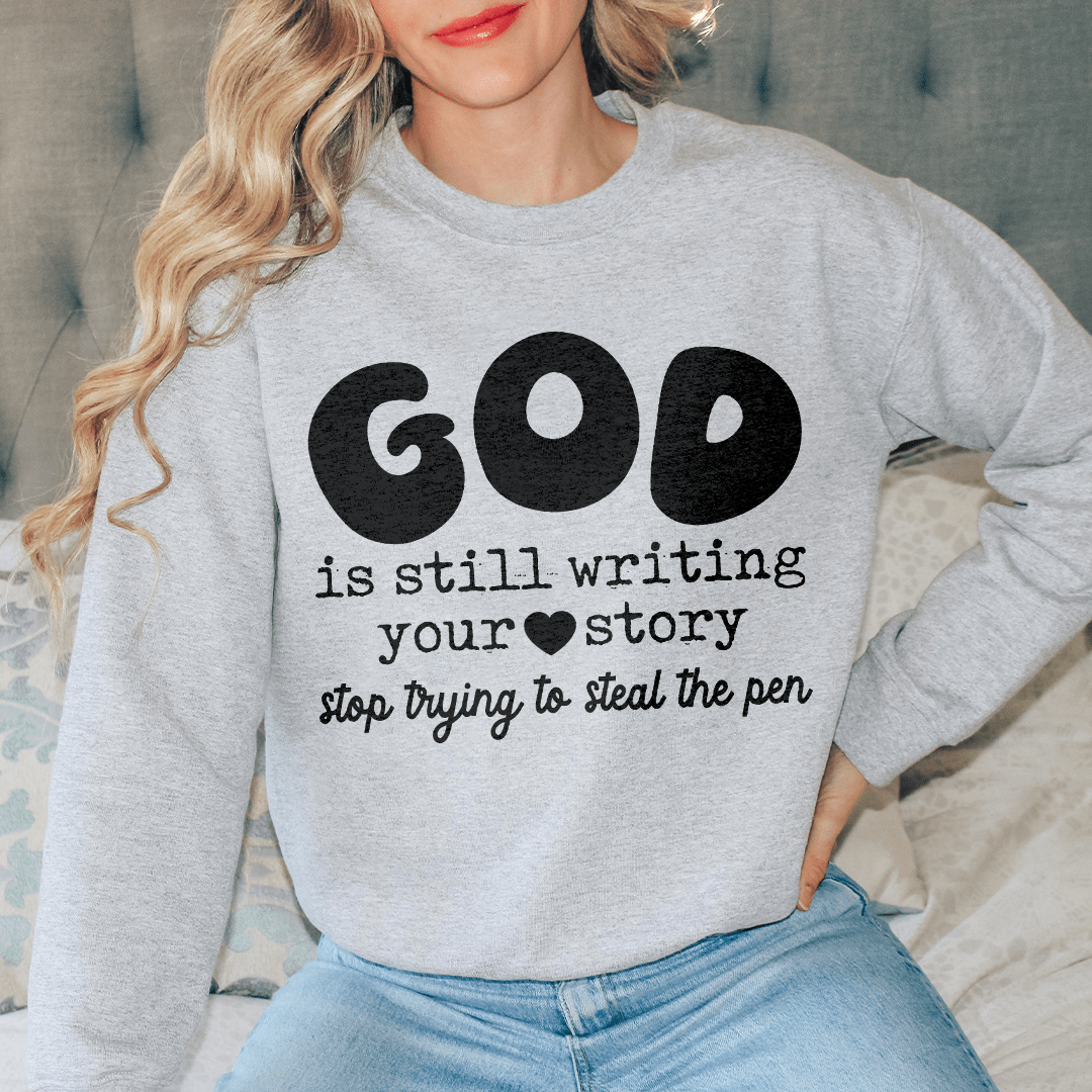 A cozy sweatshirt featuring the phrase 'God Is Still Writing Your Story', designed by top artists, made from a warm cotton/poly fleece blend.