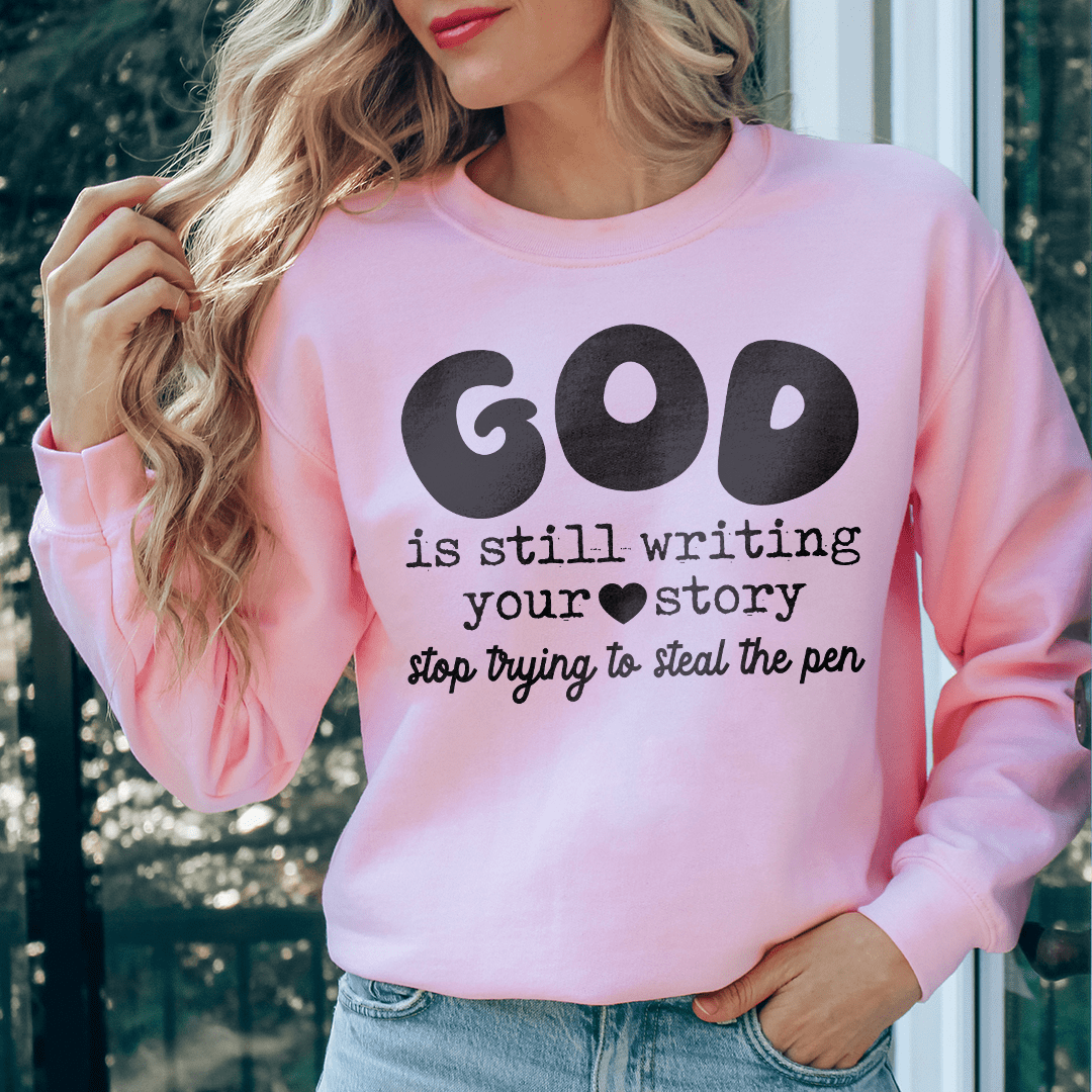 A cozy sweatshirt featuring the phrase 'God Is Still Writing Your Story', designed by top artists, made from a warm cotton/poly fleece blend.