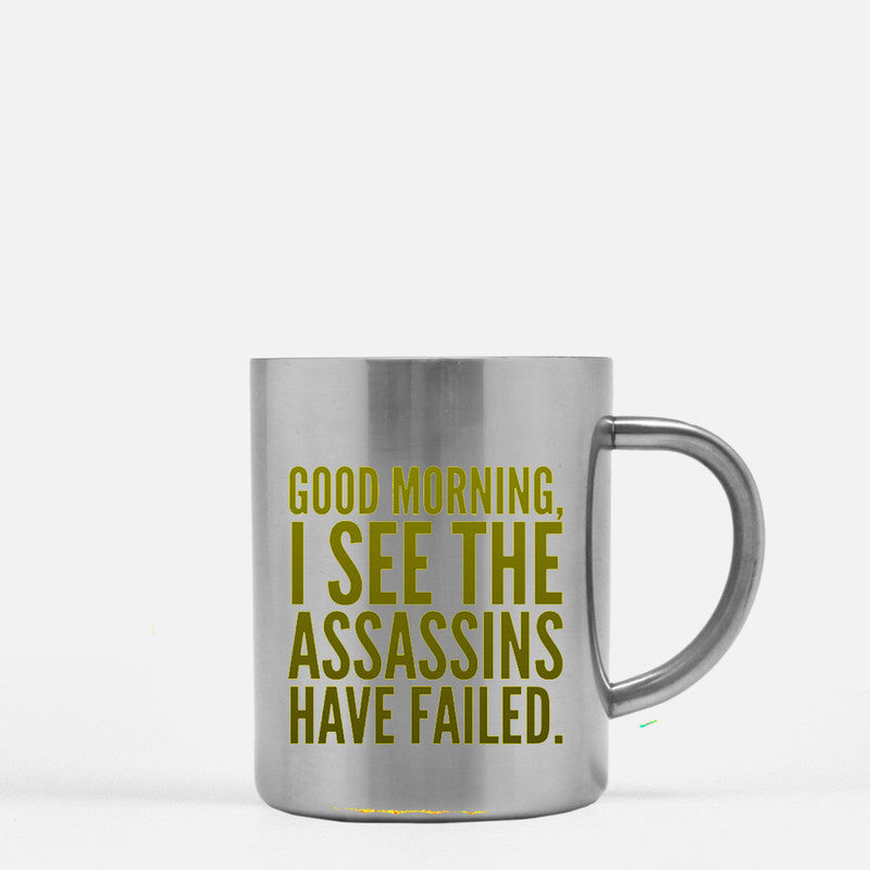 Ceramic mug with gold metallic coating featuring the phrase 'Good Morning I See The Assassins Have Failed' on one or both sides.