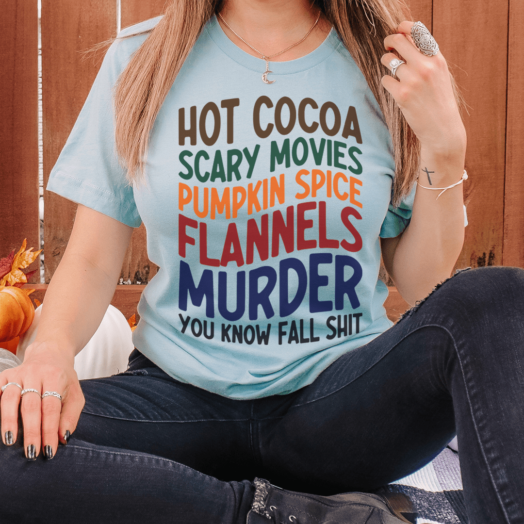 A cozy t-shirt featuring a fun design with hot cocoa, scary movies, and pumpkin spice themes, perfect for fall.