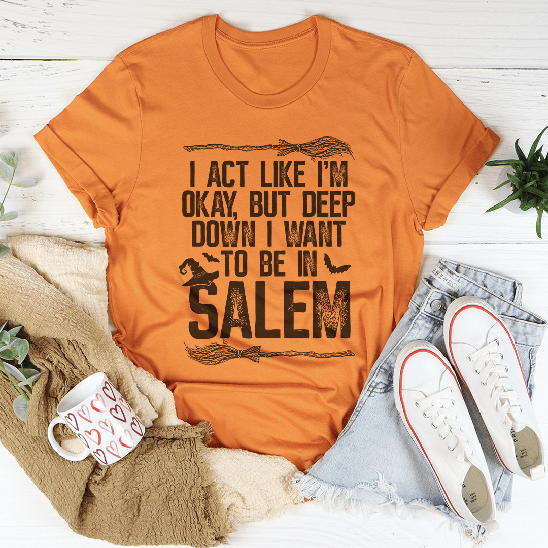 A stylish black t-shirt with the phrase 'I Act Like I'm Okay But Deep Down I Want To Be In Salem' printed in white, showcasing its comfortable fit and durable design.