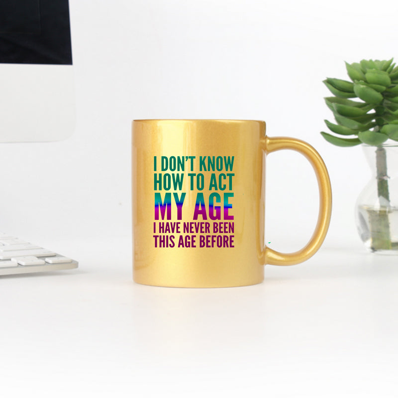 Gold ceramic mug with the phrase 'I Don't Know How To Act My Age' printed on it, showcasing a playful design.