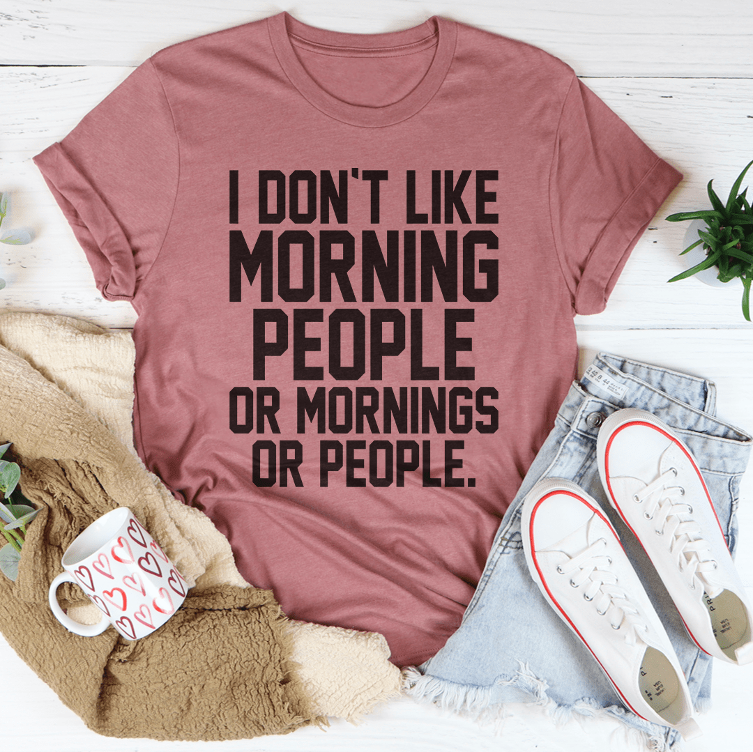 A black t-shirt with the phrase 'I Don't Like Morning People Or Mornings Or People' printed in bold white letters, showcasing a casual and humorous design.