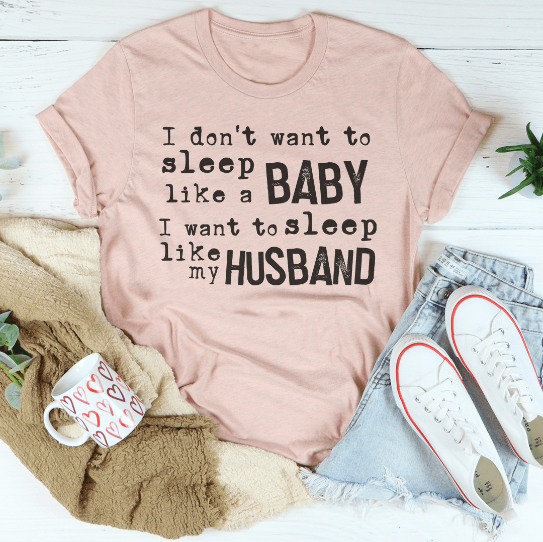 A humorous t-shirt featuring the phrase 'I Don't Want To Sleep Like A Baby I Want To Sleep Like My Husband', made from soft cotton.