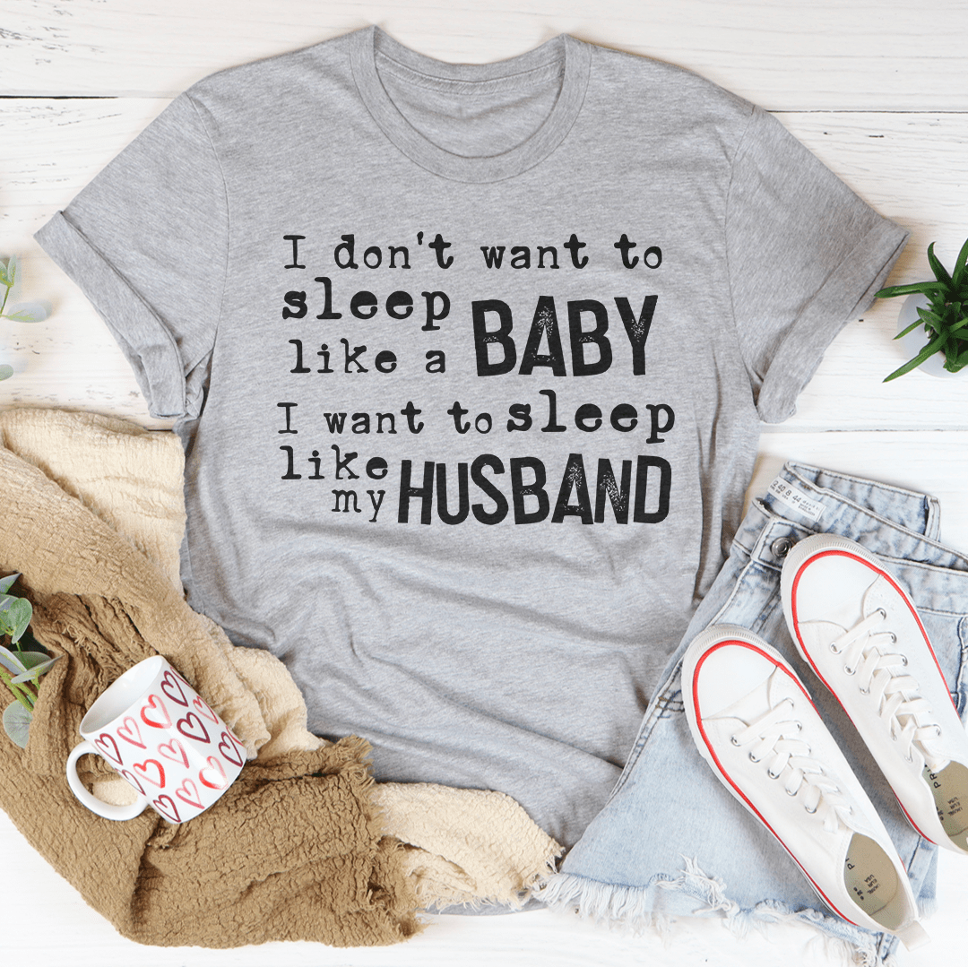 A humorous t-shirt featuring the phrase 'I Don't Want To Sleep Like A Baby I Want To Sleep Like My Husband', made from soft cotton.