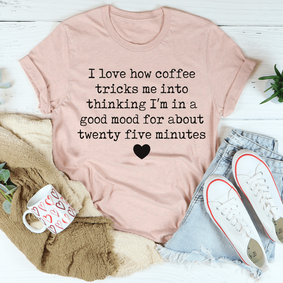 A comfortable t-shirt featuring the phrase 'I Love How Coffee Tricks Me Into Thinking I'm In A Good Mood', made from soft ring-spun cotton.