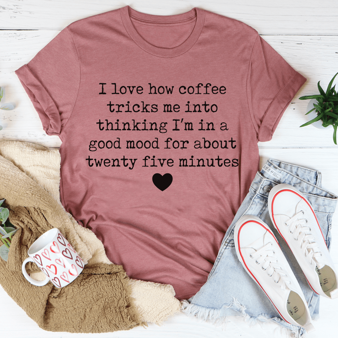 A comfortable t-shirt featuring the phrase 'I Love How Coffee Tricks Me Into Thinking I'm In A Good Mood', made from soft ring-spun cotton.