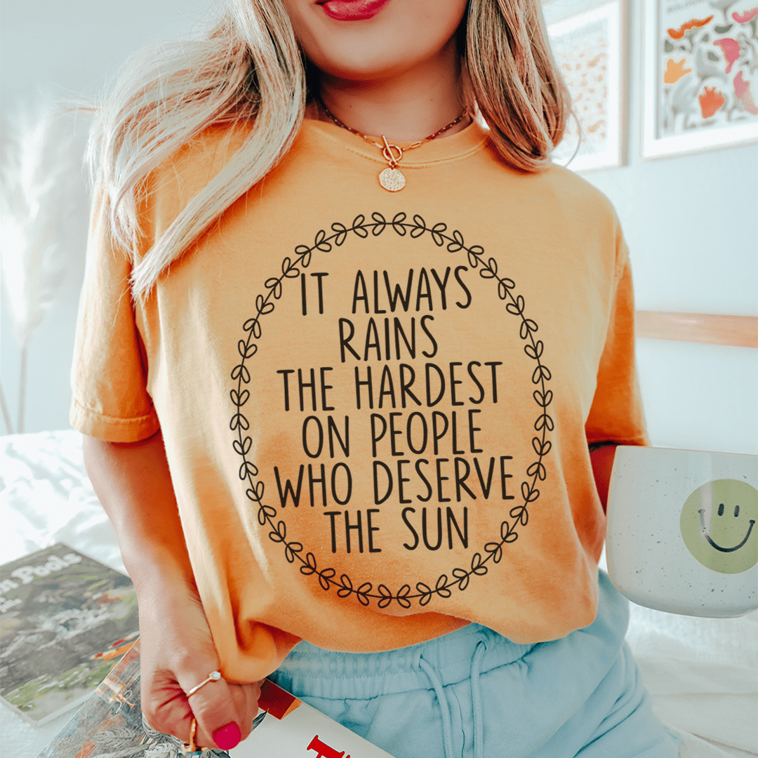 A soft, durable t-shirt featuring the phrase 'It Always Rains The Hardest On People Who Deserve The Sun' printed in vibrant colors.