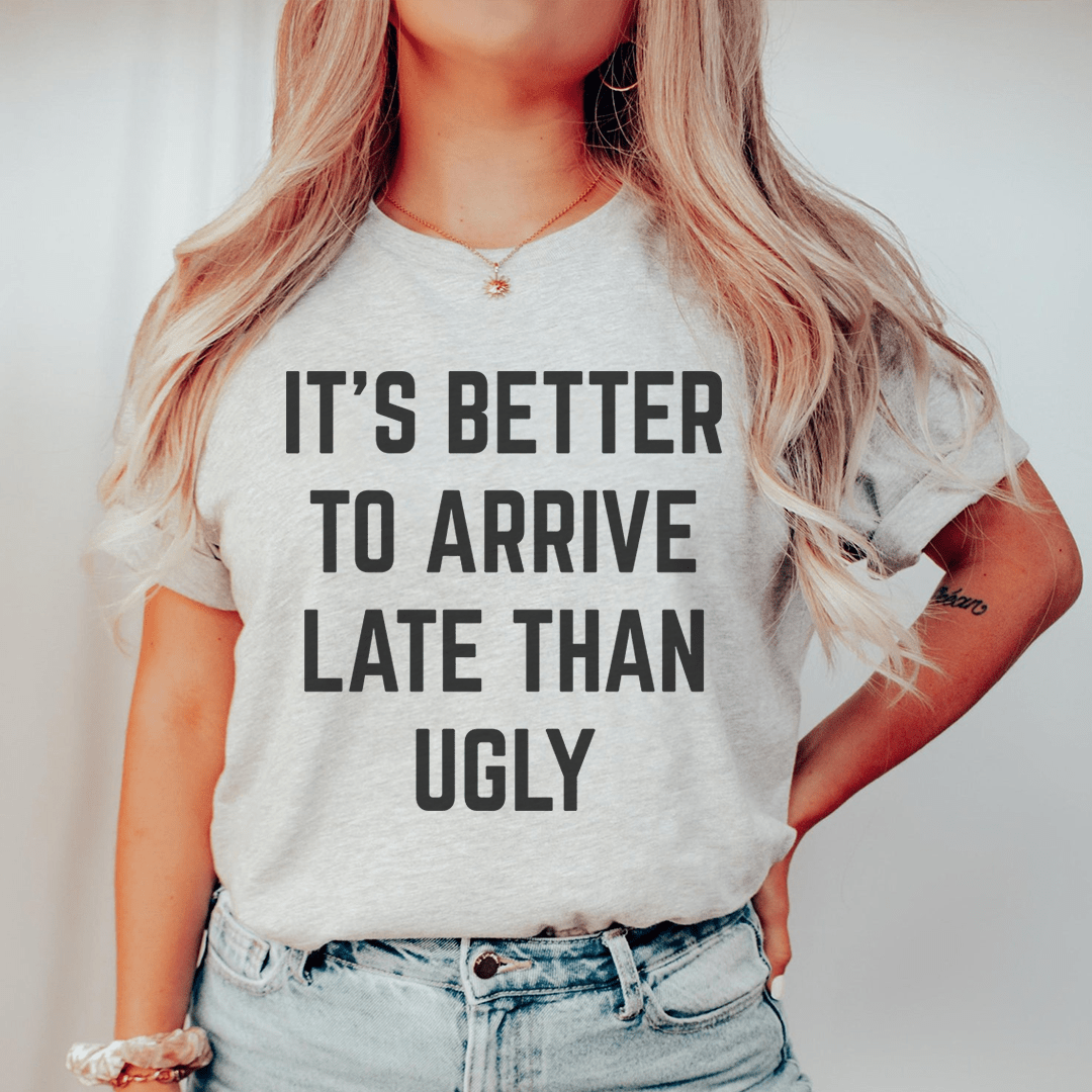 A stylish black t-shirt featuring the phrase 'It's Better To Arrive Late Than Ugly' in bold lettering, made from soft cotton fabric.