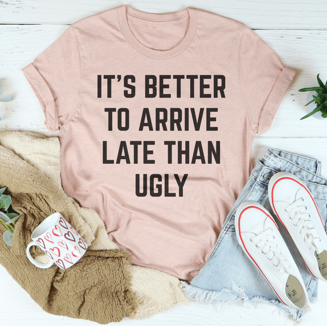 A stylish black t-shirt featuring the phrase 'It's Better To Arrive Late Than Ugly' in bold lettering, made from soft cotton fabric.