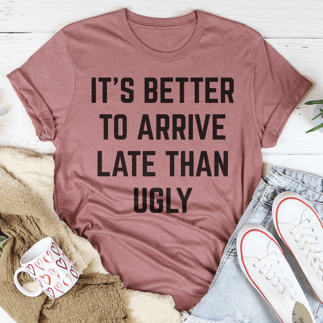 A stylish black t-shirt featuring the phrase 'It's Better To Arrive Late Than Ugly' in bold lettering, made from soft cotton fabric.