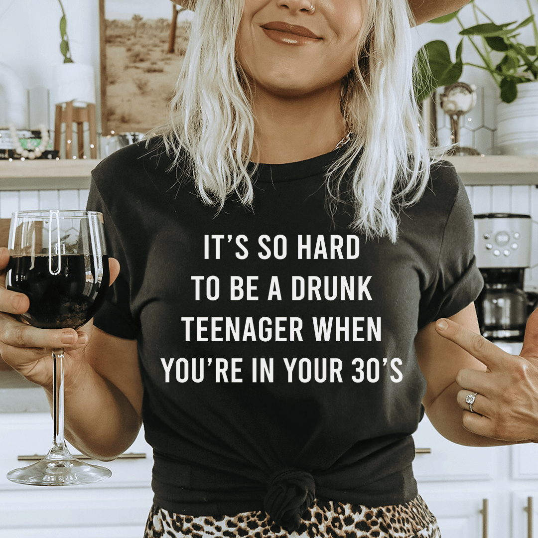 A stylish t-shirt featuring the phrase 'It's So Hard To Be A Drunk Teenager When You're In Yours 30's', made from soft cotton with double stitching.