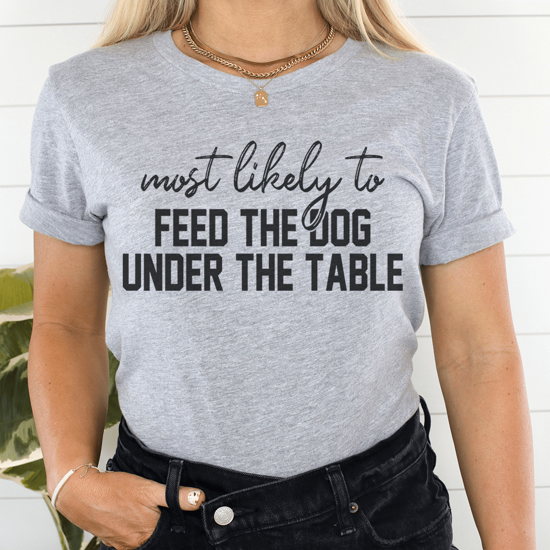 A comfortable Thanksgiving t-shirt featuring the phrase 'Most Likely To Feed The Dog Under The Table' in a playful design.