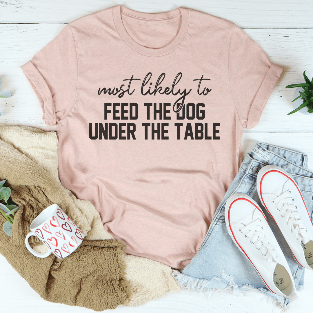 A comfortable Thanksgiving t-shirt featuring the phrase 'Most Likely To Feed The Dog Under The Table' in a playful design.