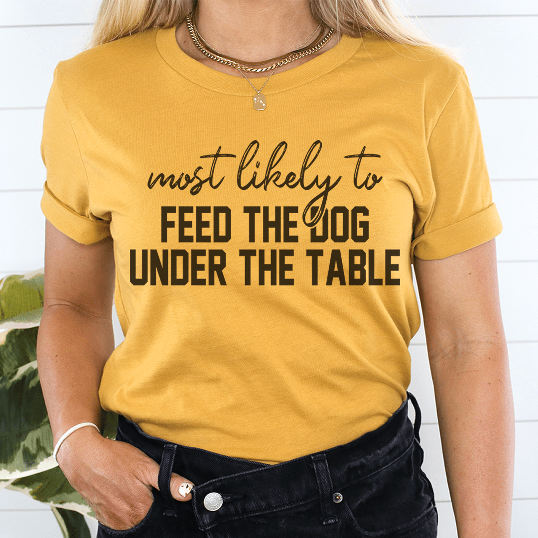 A comfortable Thanksgiving t-shirt featuring the phrase 'Most Likely To Feed The Dog Under The Table' in a playful design.