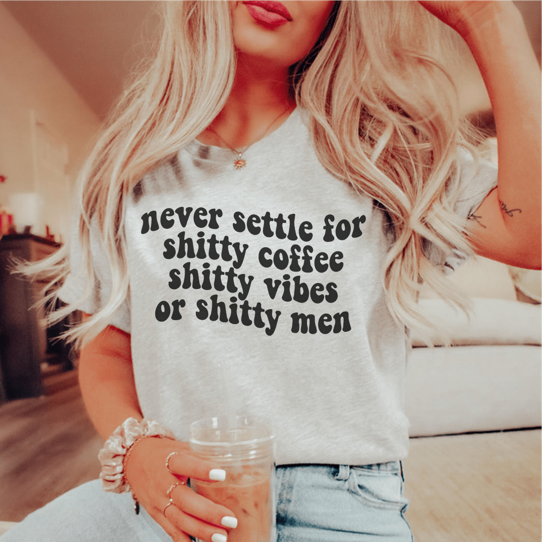 A stylish black t-shirt with the phrase 'Never Settle For Shitty Coffee' printed in bold white letters, showcasing its comfortable fabric and durable stitching.