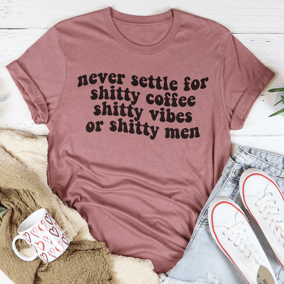 A stylish black t-shirt with the phrase 'Never Settle For Shitty Coffee' printed in bold white letters, showcasing its comfortable fabric and durable stitching.