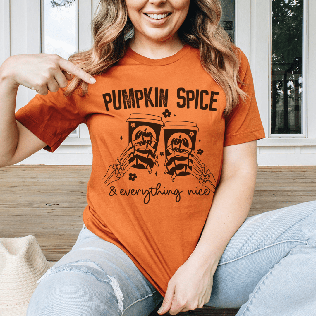 Pumpkin Spice & Everything Nice T-Shirt displayed on a wooden background, showcasing its soft fabric and vibrant autumn-themed design.