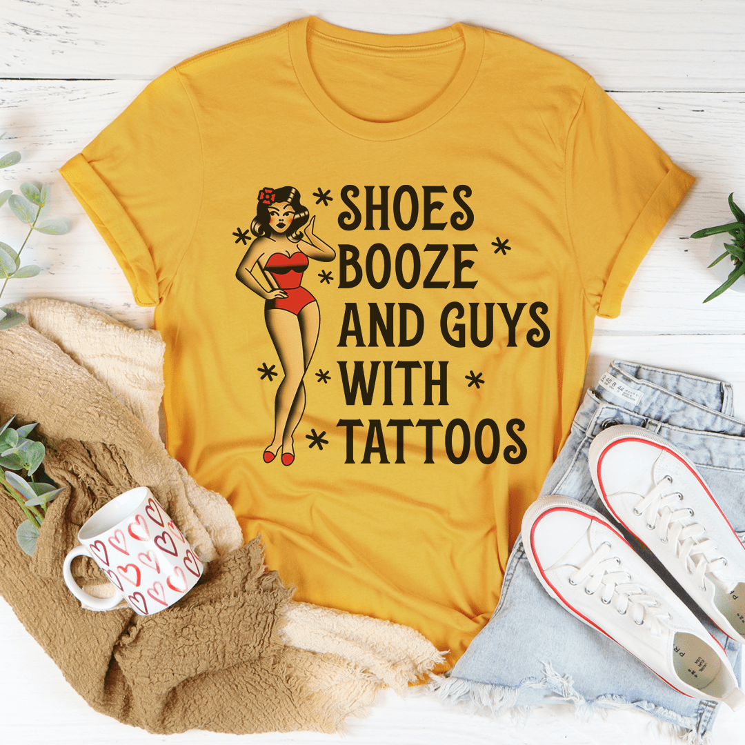 A stylish black t-shirt featuring the phrase 'Shoes Booze And Guys With Tattoos' printed in bold letters, showcasing its comfortable fabric and double stitching.