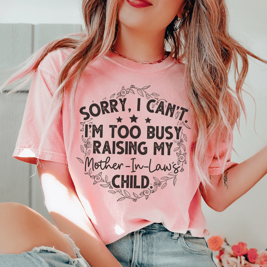 A humorous t-shirt featuring the phrase 'Sorry I Can't I'm Too Busy Raising My Mother In Law's Child', made of soft cotton.