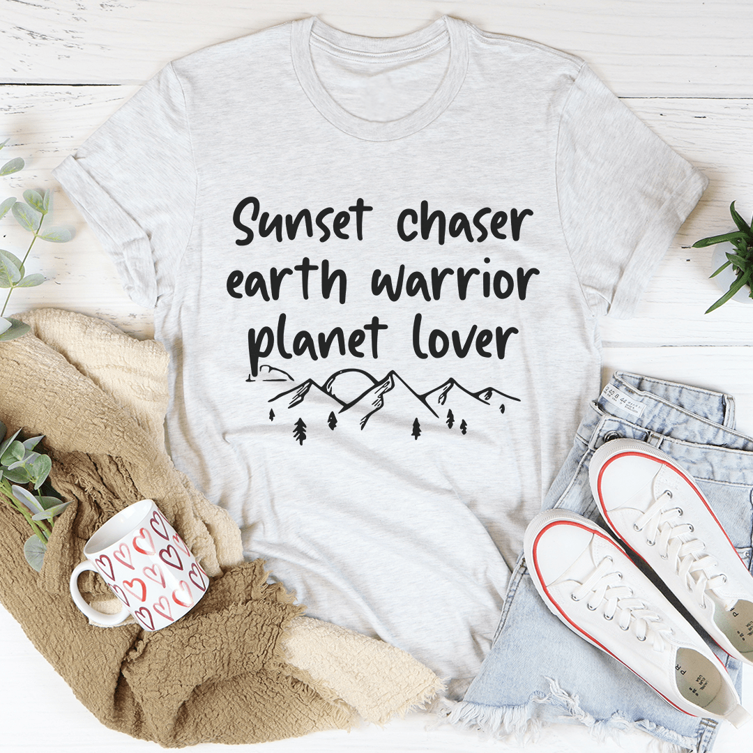 Sunset Chaser Earth Warrior Planet Lover Tee displayed on a wooden background, showcasing its soft cotton fabric and double-stitched neckline.