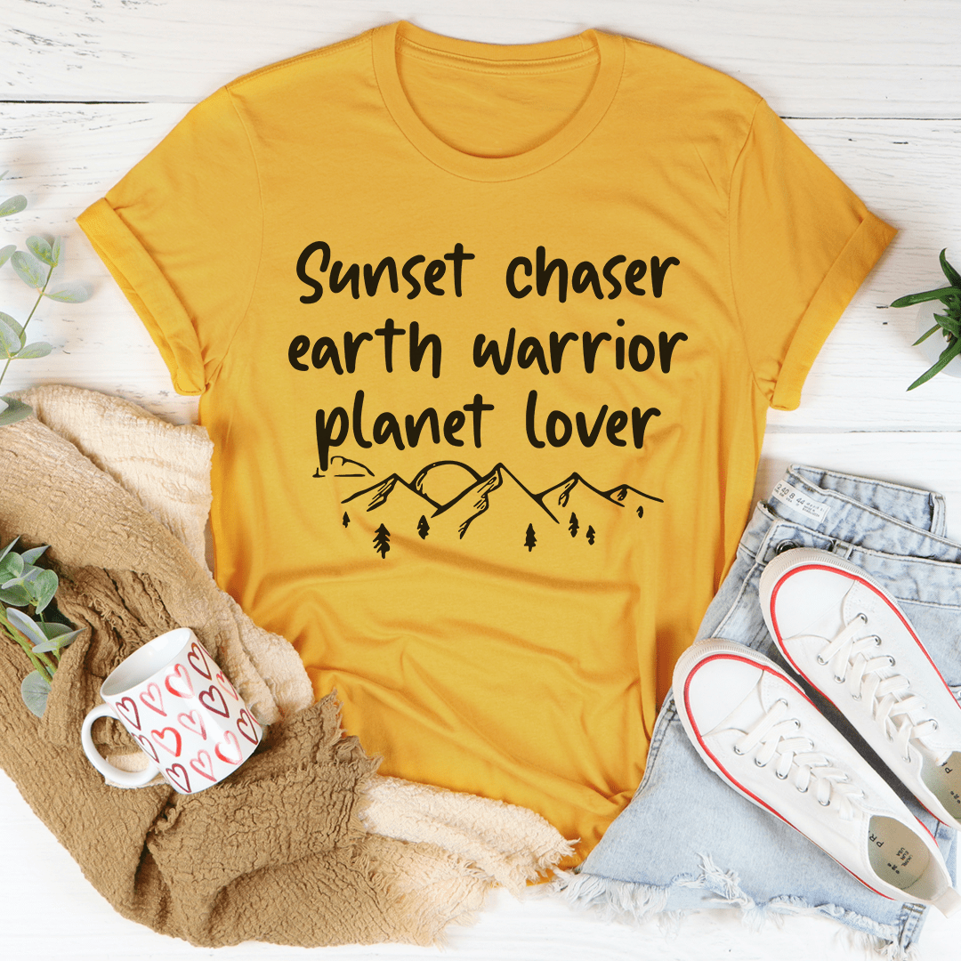 Sunset Chaser Earth Warrior Planet Lover Tee displayed on a wooden background, showcasing its soft cotton fabric and double-stitched neckline.