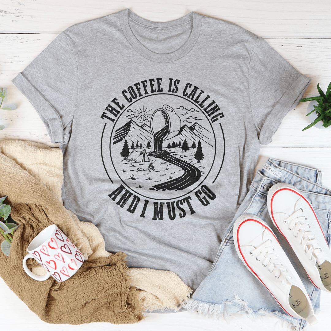 A stylish t-shirt featuring the phrase 'The Coffee Is Calling And I Must Go', made from soft ring-spun cotton with double stitching for durability.