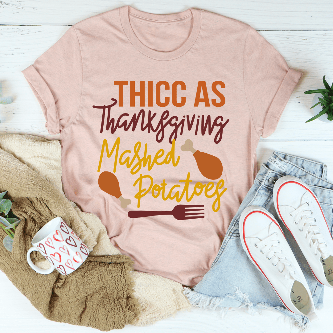 Thicc As Thanksgiving Mashed Potatoes T-Shirt displayed on a hanger, showcasing its soft cotton fabric and double stitching.