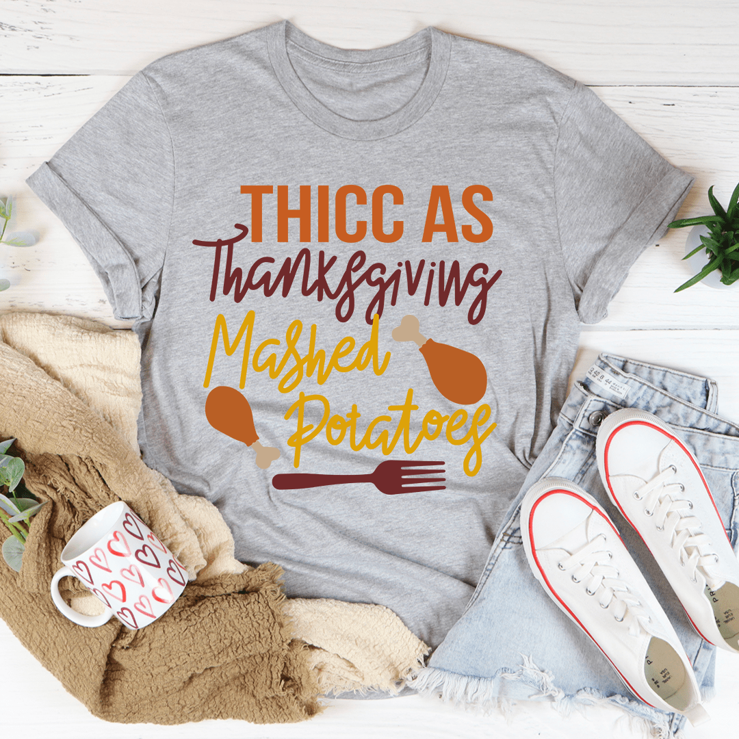 Thicc As Thanksgiving Mashed Potatoes T-Shirt displayed on a hanger, showcasing its soft cotton fabric and double stitching.