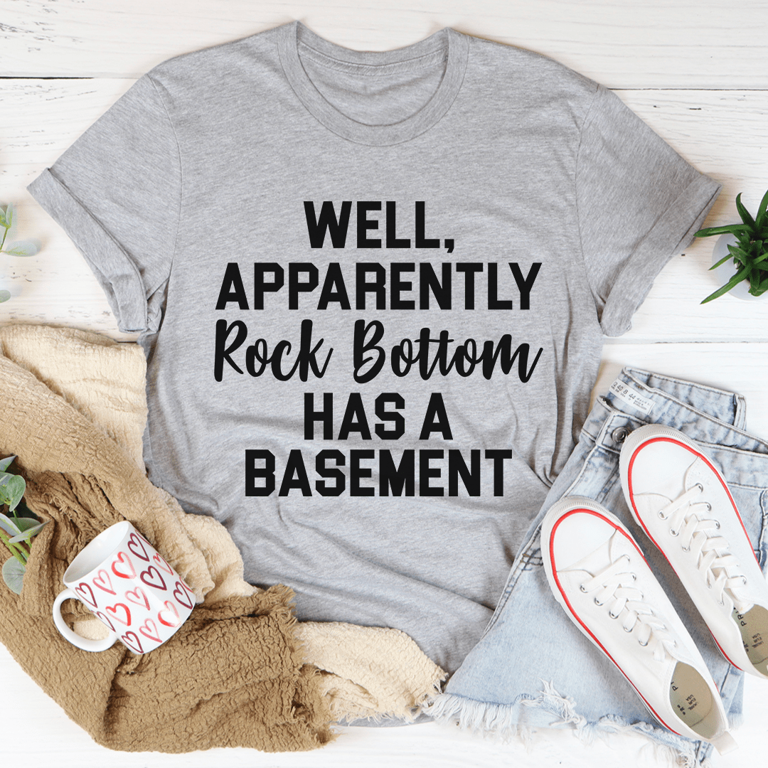 A stylish t-shirt featuring the phrase 'Well Apparently Rock Bottom Has A Basement', made from soft ring-spun cotton with double stitching.