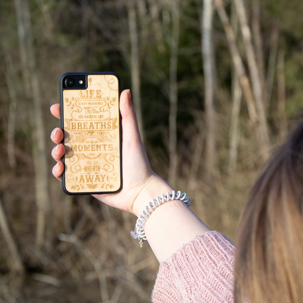 The Meaning wooden phone case displayed outdoors, showcasing its unique grain and design, held by a woman in a natural setting.