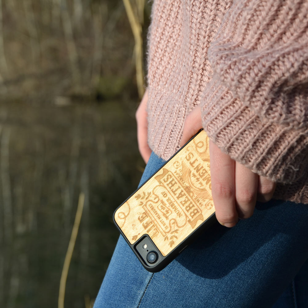 The Meaning wooden phone case displayed outdoors, showcasing its unique grain and design, held by a woman in a natural setting.