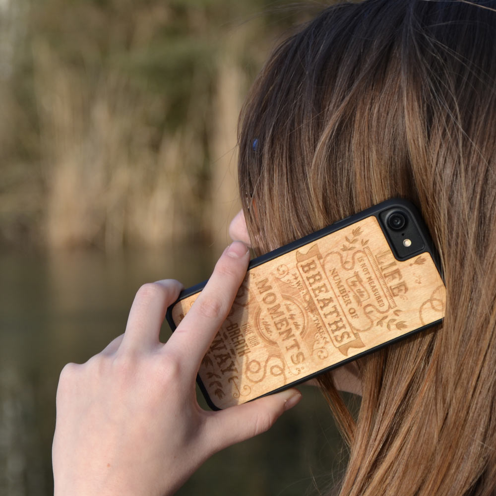 The Meaning wooden phone case displayed outdoors, showcasing its unique grain and design, held by a woman in a natural setting.