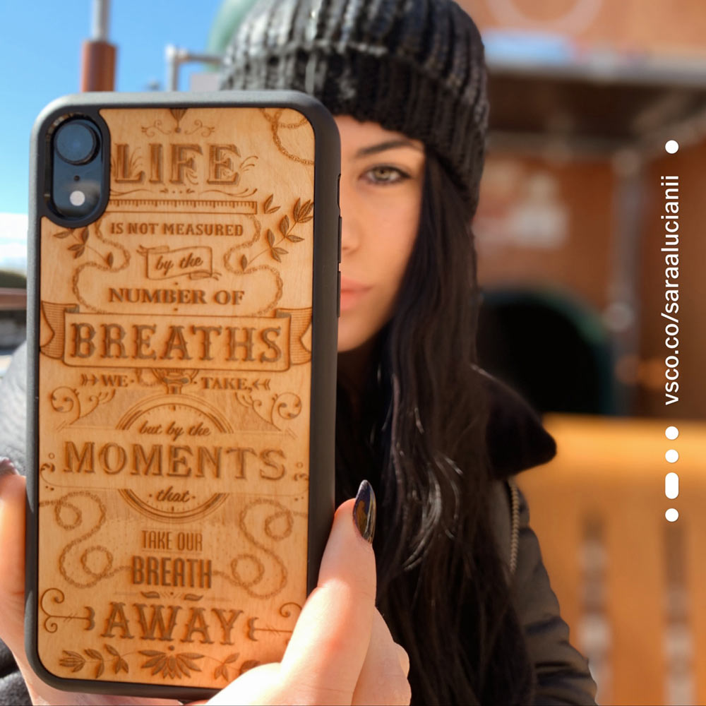 The Meaning wooden phone case displayed outdoors, showcasing its unique grain and design, held by a woman in a natural setting.