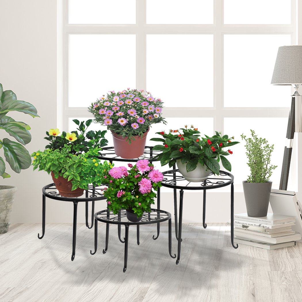 Four black metal plant stands arranged with various flower pots, showcasing an elegant outdoor and indoor decor.