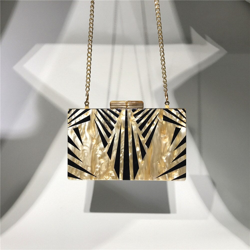 Acrylic luxury evening bag with a golden metal chain shoulder strap, featuring a stylish striped pattern and flap design.