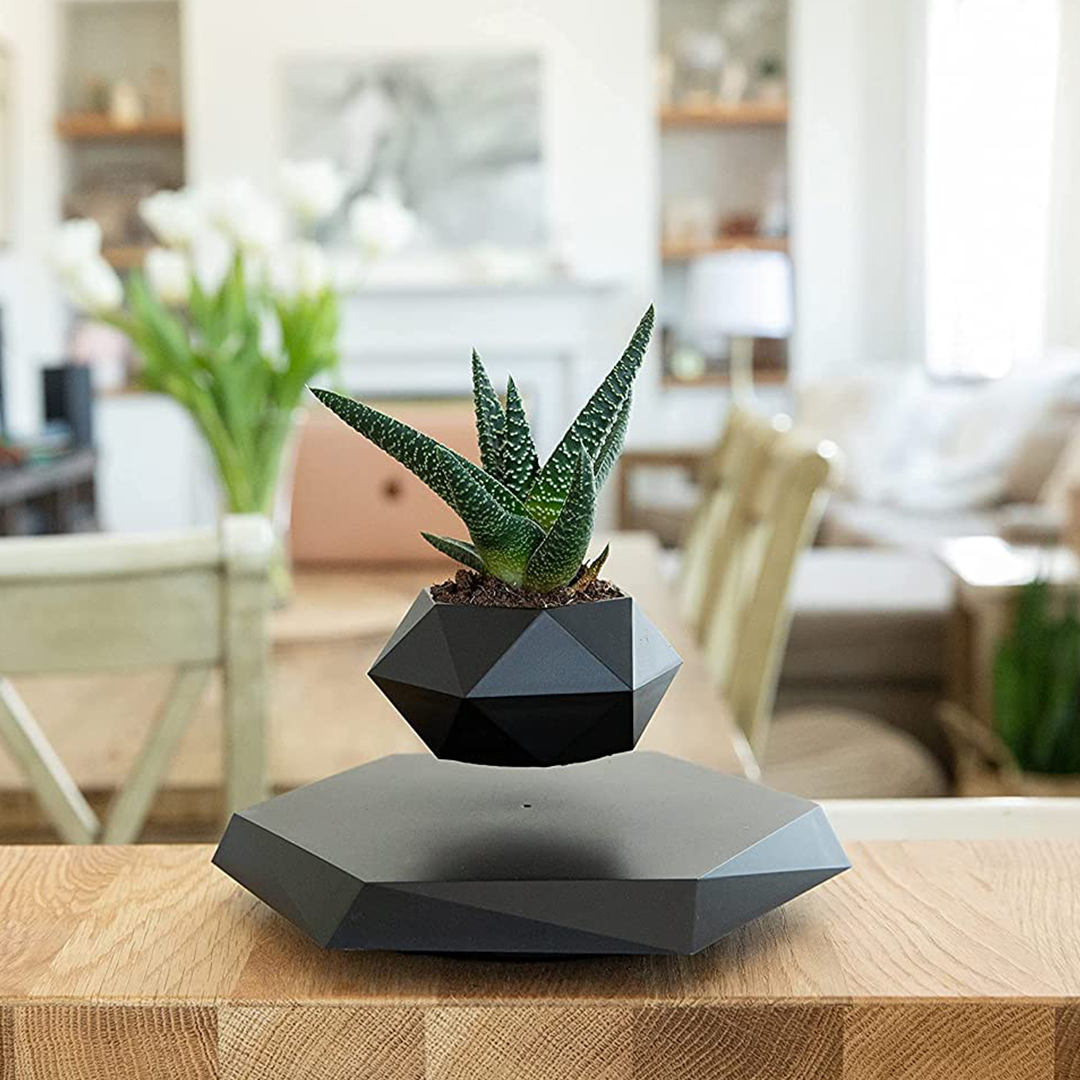 A black geometric levitating plant pot showcasing a small plant floating in mid-air, rotating smoothly above its magnetic base.