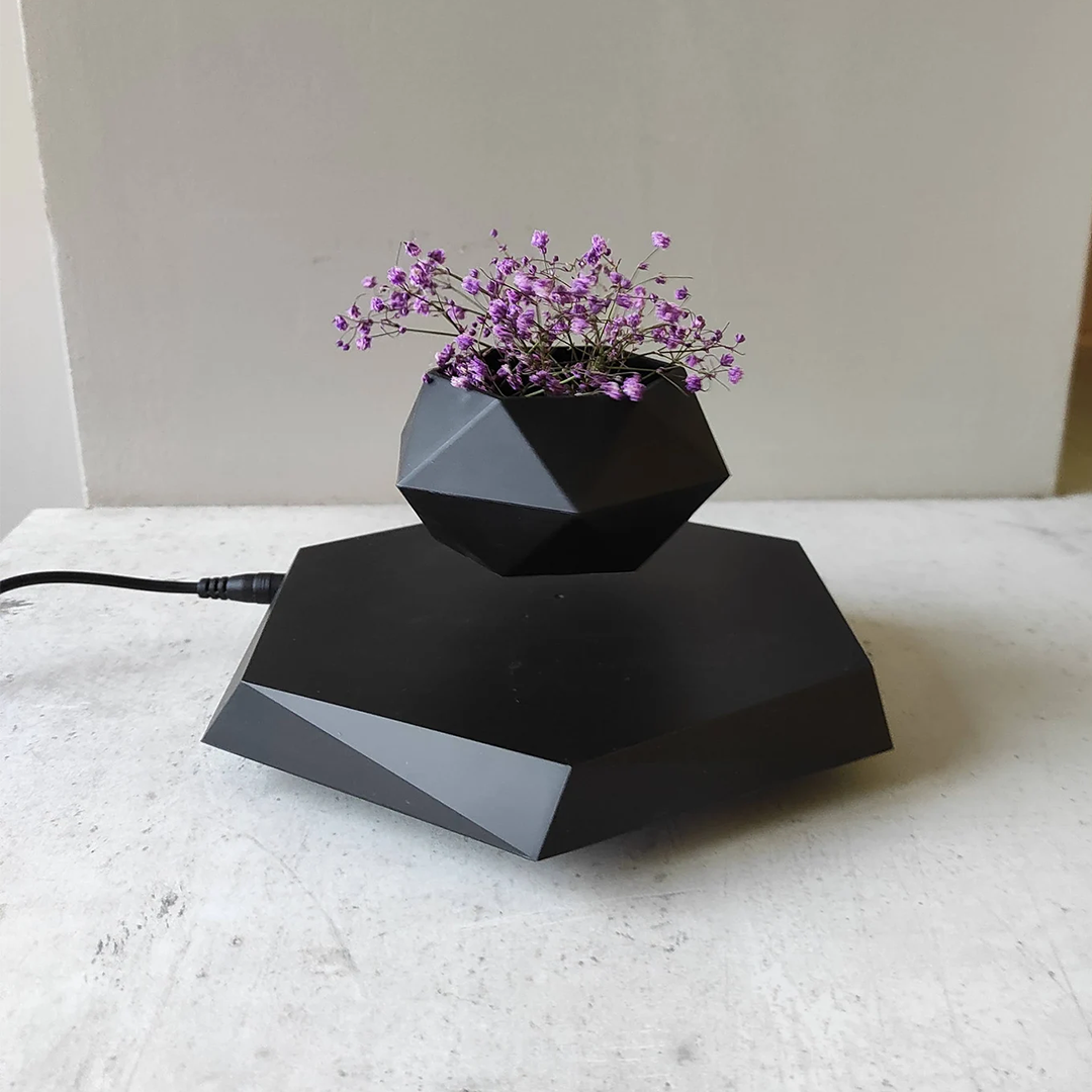 A black geometric levitating plant pot showcasing a small plant floating in mid-air, rotating smoothly above its magnetic base.