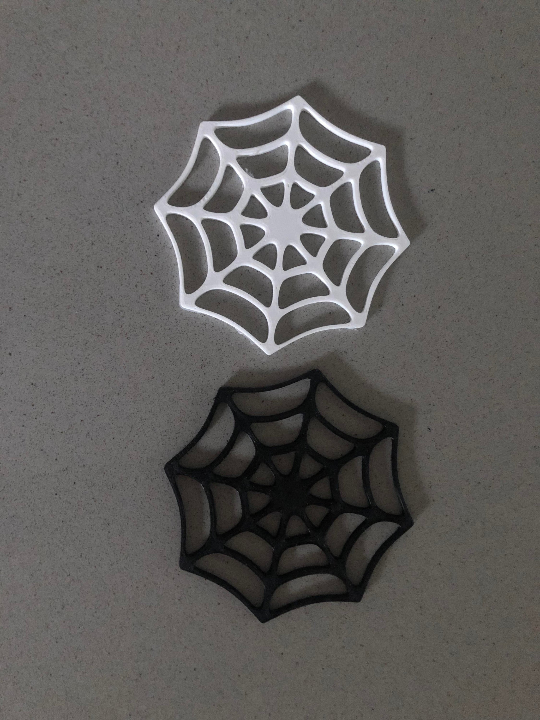 A set of four Halloween-themed coasters featuring intricate cobweb designs in black and white colors, perfect for holding cups and mugs.