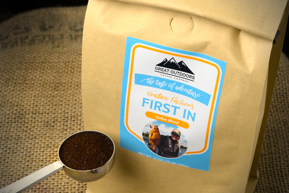 A steaming cup of First In coffee by Kristine Fischer, showcasing its rich color and inviting aroma, set against a serene outdoor backdrop.