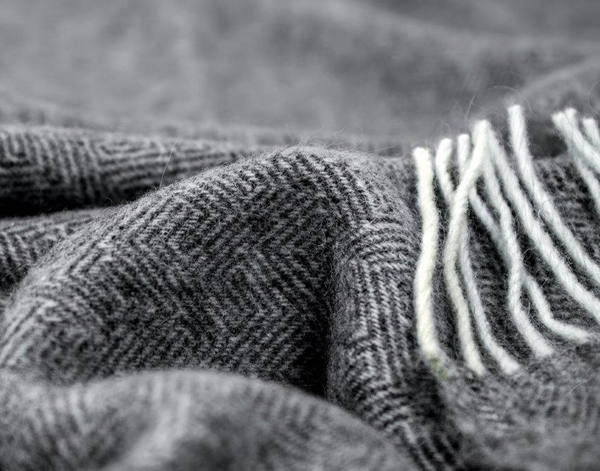 Hampton Throw blanket in dark grey, made from a luxurious Merino wool blend, elegantly draped over a cozy sofa.