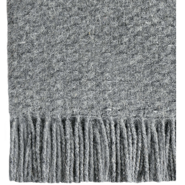 Soho Throw blanket in grey, made from a wool blend, elegantly draped on a cozy couch, showcasing its soft texture and stylish design.