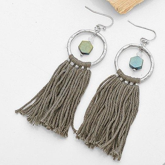 A pair of Tassela Trendy Earrings featuring olive and tan tassels, onyx and crystal accents, and a hammered gold finish.