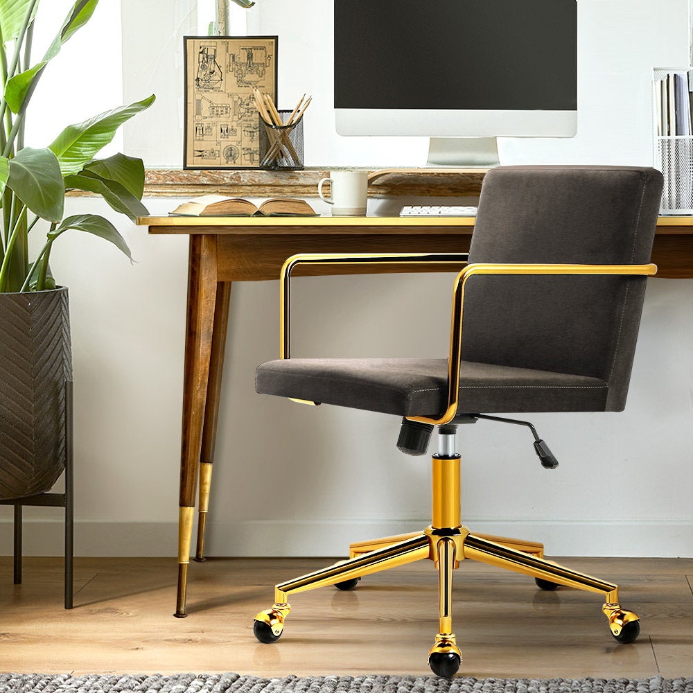 Caraway Velvet Office Chair with metallic brass base and armrests, showcasing luxurious charcoal upholstery and smooth castor wheels.